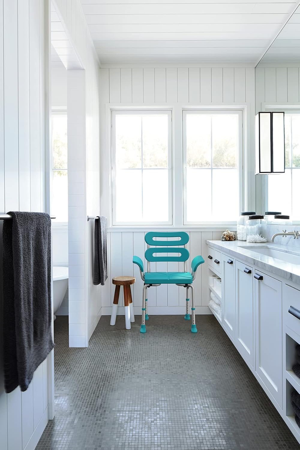 Bathroom with teal chair, white vanity, and large windows.