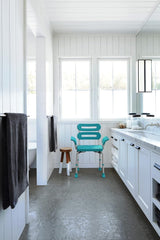 Bathroom with teal chair, white vanity, and large windows.